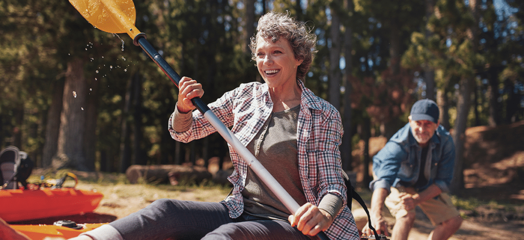 Mature couple kayaking on a peaceful lake while enjoying an active outdoor lifestyle with waterproof hearing aids